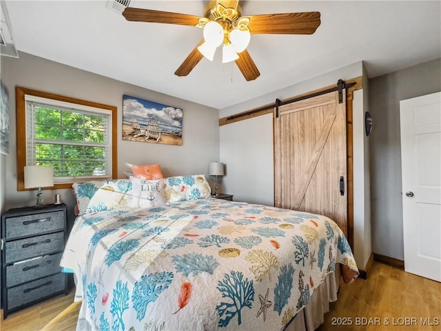 bedroom with light wood-type flooring, a barn door, ceiling fan, and baseboards