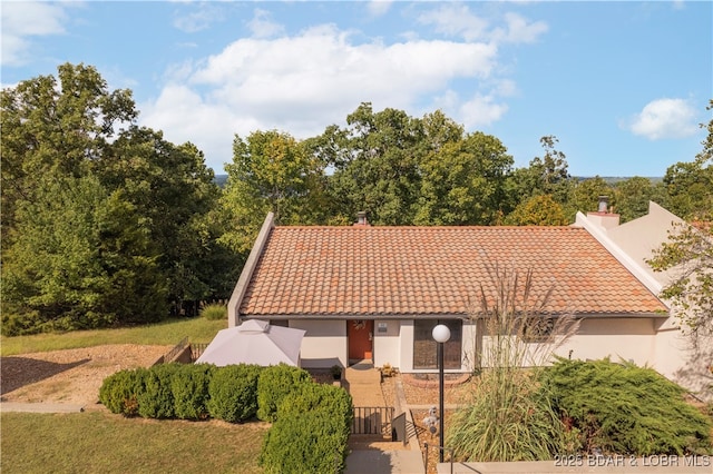 view of front of home featuring stucco siding, a tile roof, and a chimney