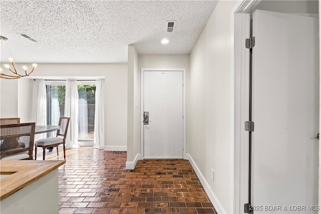 entryway with baseboards, a textured ceiling, and a chandelier