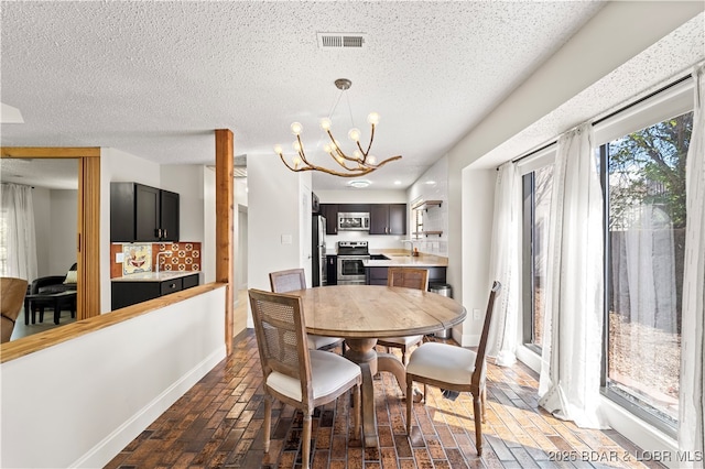 dining space featuring a chandelier, a textured ceiling, brick floors, and baseboards