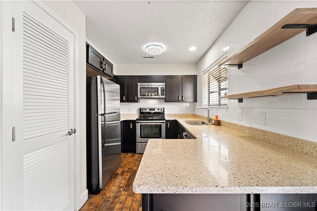 kitchen featuring open shelves, stainless steel appliances, a sink, a textured ceiling, and light stone countertops