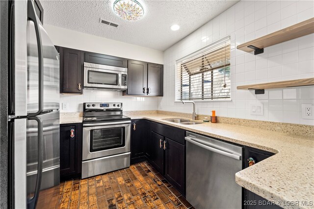 kitchen with stainless steel appliances, a sink, open shelves, backsplash, and a textured ceiling