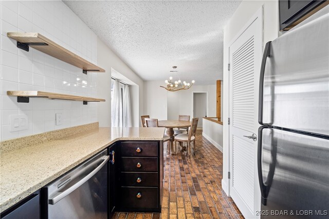kitchen featuring appliances with stainless steel finishes, open shelves, brick flooring, a chandelier, and light stone countertops