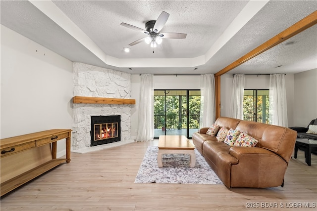 living room with a textured ceiling, healthy amount of natural light, a raised ceiling, a ceiling fan, and a fireplace