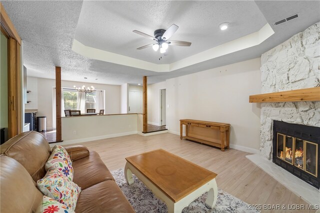 living room featuring a textured ceiling, a tray ceiling, a stone fireplace, light wood-style floors, and a chandelier