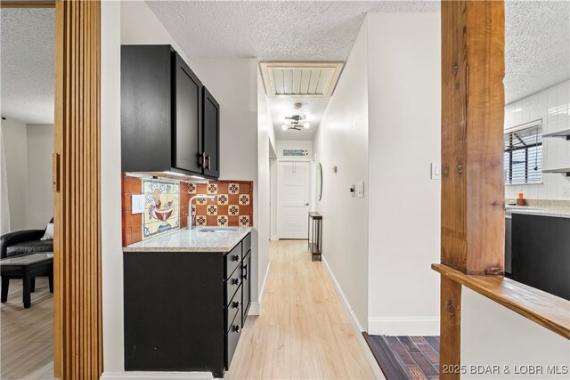 corridor with a textured ceiling, a sink, attic access, light wood-type flooring, and baseboards