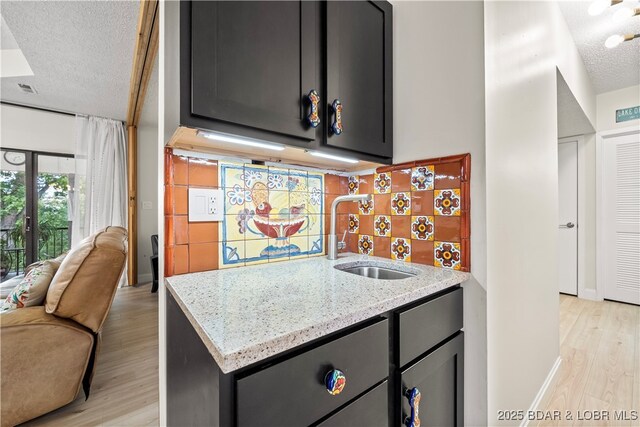 kitchen with a sink, tasteful backsplash, light wood-style flooring, light stone countertops, and a textured ceiling