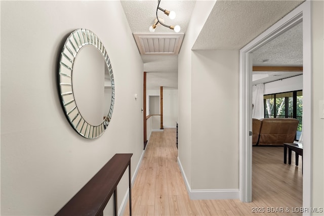 hallway with a textured ceiling, light wood-style flooring, baseboards, and rail lighting