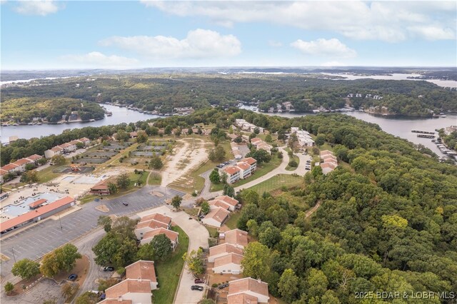 aerial view of property and surrounding area featuring a nearby body of water and a heavily wooded area