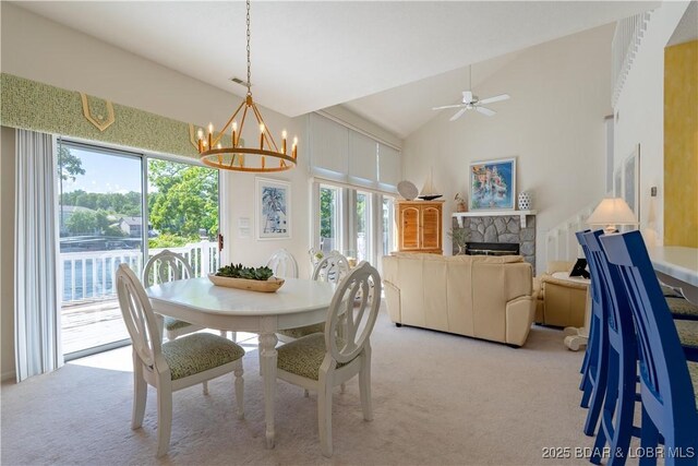 dining space with light colored carpet, a fireplace, ceiling fan, a chandelier, and vaulted ceiling