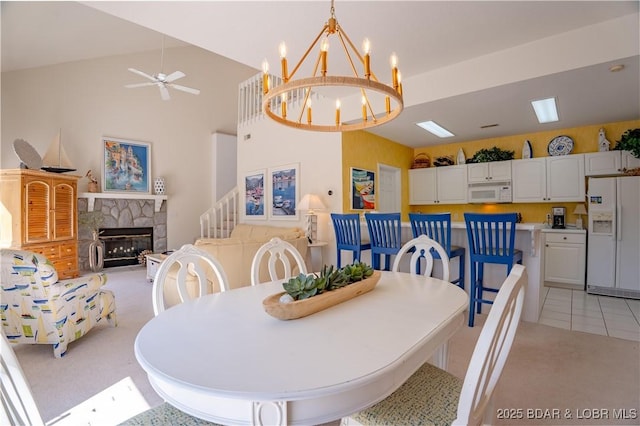 dining area featuring a fireplace, ceiling fan, a chandelier, vaulted ceiling, and light carpet