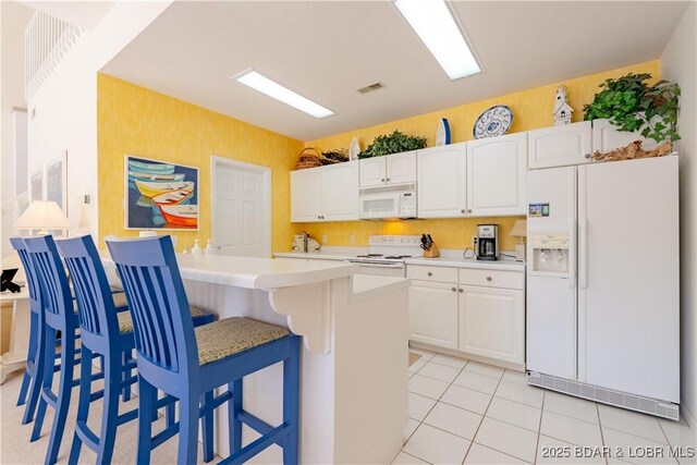 kitchen featuring white appliances, a kitchen breakfast bar, light countertops, white cabinets, and light tile patterned flooring