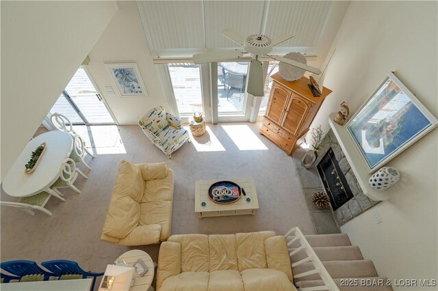 living area featuring a high ceiling, a fireplace with raised hearth, and ceiling fan