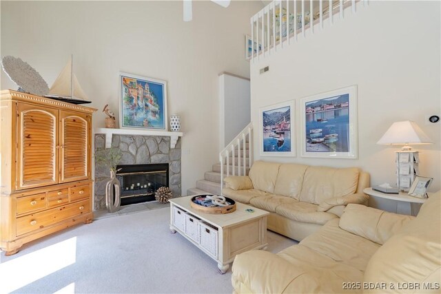 living area featuring light colored carpet, a stone fireplace, stairs, and a towering ceiling