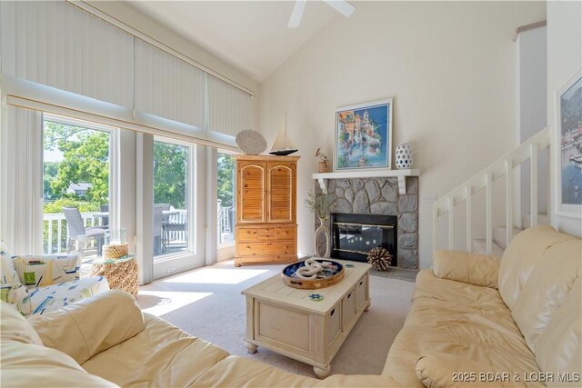 living area featuring healthy amount of natural light, light carpet, high vaulted ceiling, a stone fireplace, and stairway