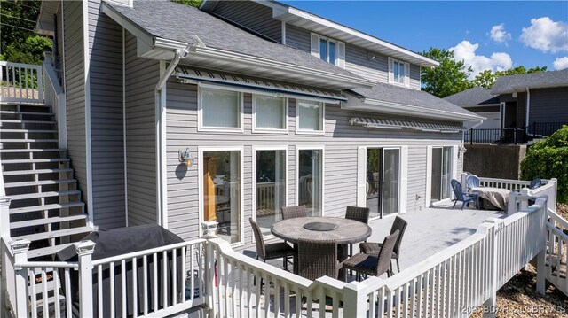 rear view of property with outdoor dining area, stairs, a shingled roof, and a wooden deck