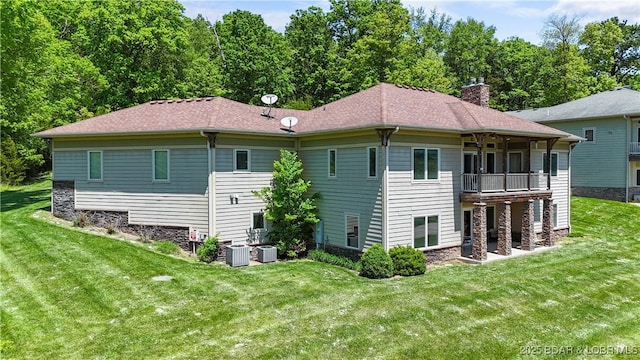 back of property featuring a balcony, a yard, a chimney, and stone siding