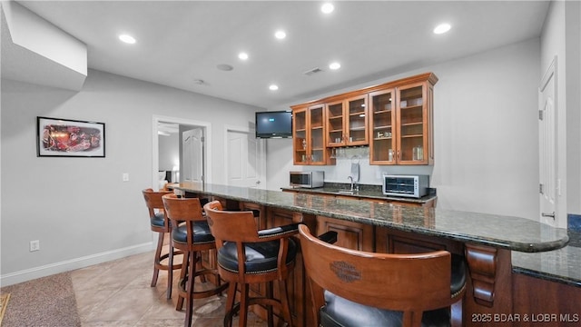 kitchen with recessed lighting, a kitchen breakfast bar, a sink, stainless steel microwave, and glass insert cabinets