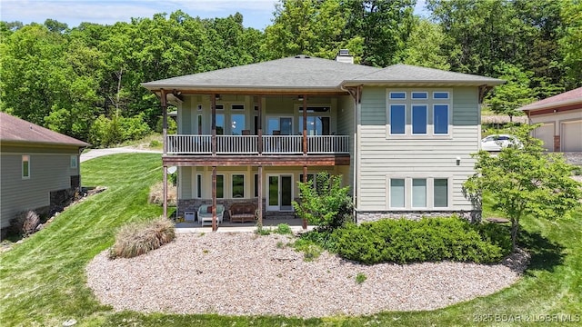 rear view of house with stone siding, a lawn, a balcony, and a chimney