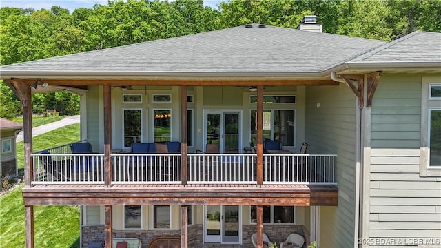 rear view of property with a ceiling fan, roof with shingles, a chimney, and stone siding