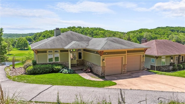 prairie-style house featuring stone siding, an attached garage, a chimney, a front yard, and concrete driveway