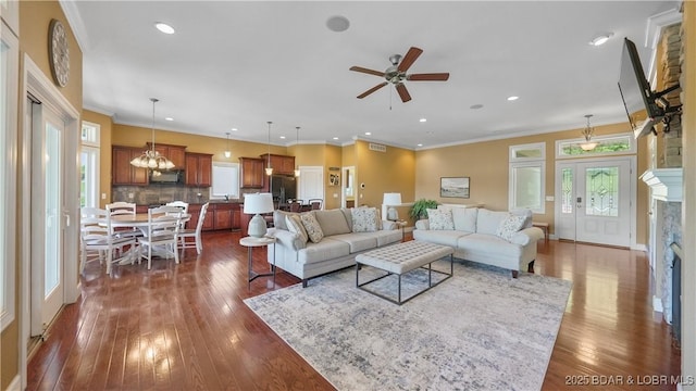 living area featuring a fireplace, dark wood-type flooring, recessed lighting, a ceiling fan, and crown molding