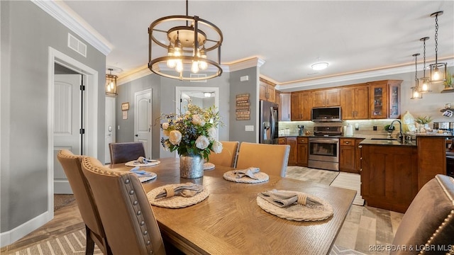 dining space featuring crown molding, light wood finished floors, a chandelier, and baseboards