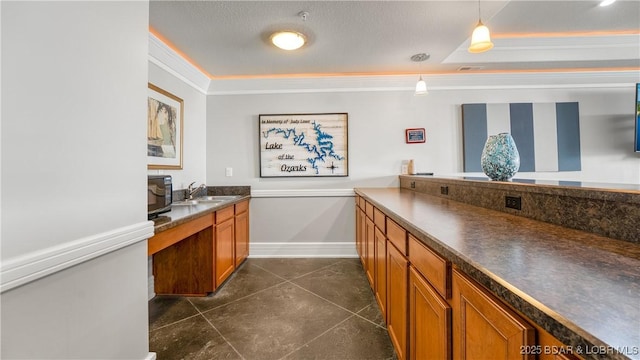 kitchen featuring a sink, ornamental molding, brown cabinetry, dark countertops, and decorative light fixtures