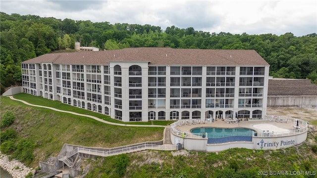 view of building exterior with a community pool, a forest view, and fence
