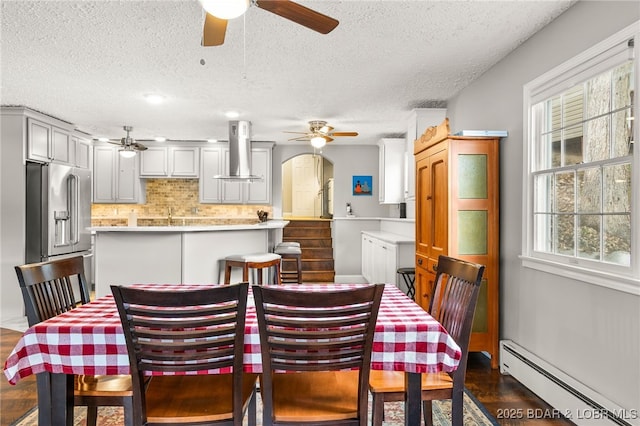 12 Mimosa Rd, Rocky Mount, MO 65072 - dining space with a baseboard radiator, a ceiling fan, a textured ceiling, arched walkways, and dark wood-style flooring