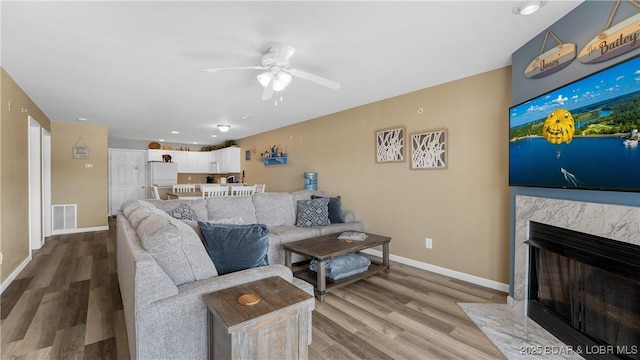 living room with ceiling fan, wood finished floors, baseboards, and a fireplace
