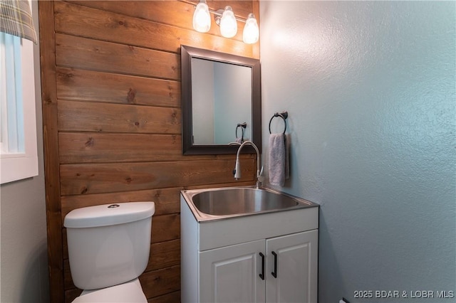 bathroom featuring toilet, vanity, and wooden walls