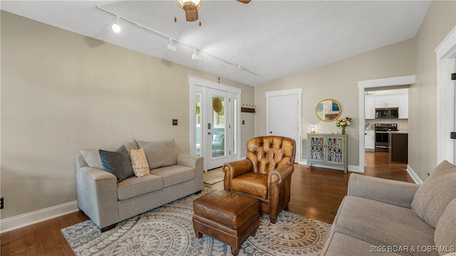 living area with track lighting, ceiling fan, wood finished floors, baseboards, and vaulted ceiling