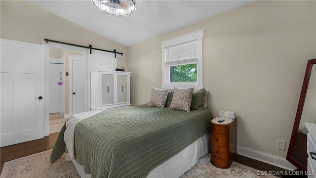 bedroom featuring a barn door, lofted ceiling, wood finished floors, and baseboards
