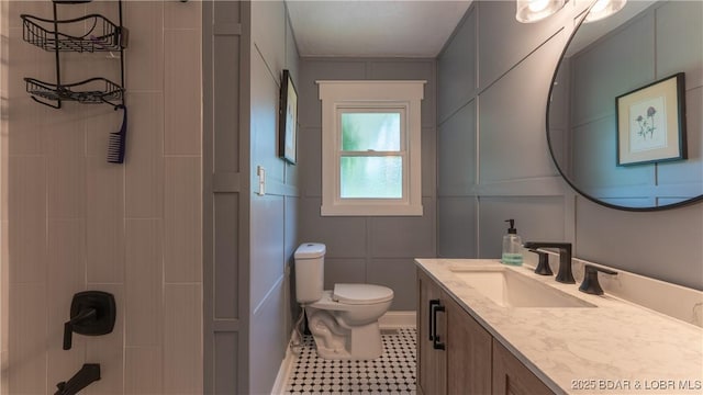 bathroom with toilet, vanity, tile patterned floors, a decorative wall, and a shower