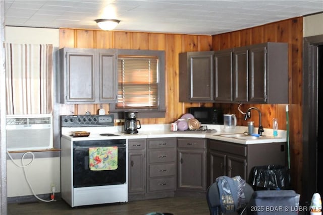 kitchen featuring white range with electric cooktop, a sink, black microwave, wooden walls, and light countertops