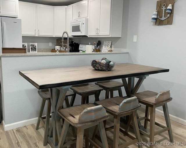 1481 Ledges Dr Unit 1019, Osage Beach, MO 65065 - kitchen featuring white microwave, baseboards, light wood finished floors, white cabinetry, and a sink