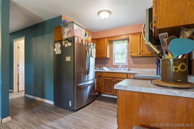 kitchen with stainless steel appliances, brown cabinets, wood finished floors, and light countertops