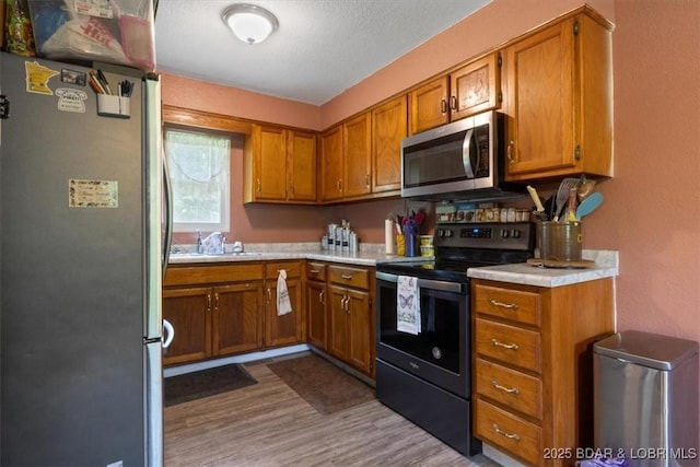 kitchen featuring appliances with stainless steel finishes, brown cabinetry, light countertops, wood finished floors, and a sink
