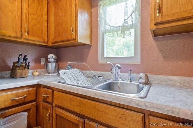 kitchen with light countertops, brown cabinets, a sink, and a textured wall