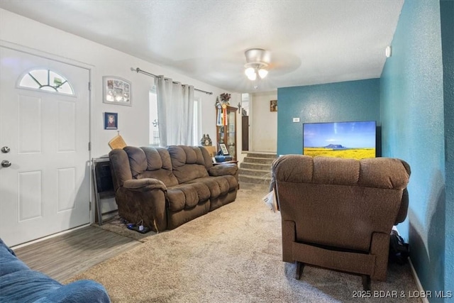 living area with healthy amount of natural light, stairs, and a ceiling fan
