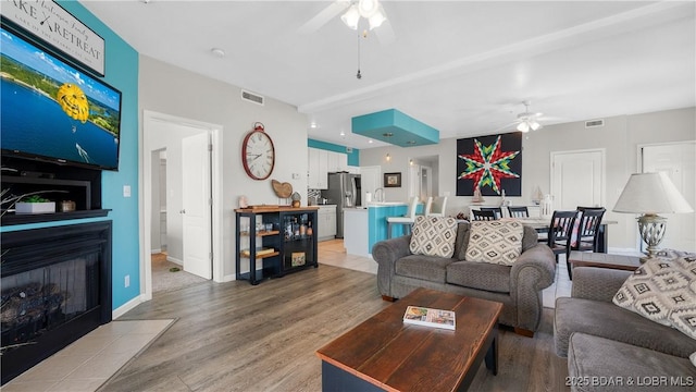 living room featuring a ceiling fan, light wood-style flooring, a fireplace, and baseboards