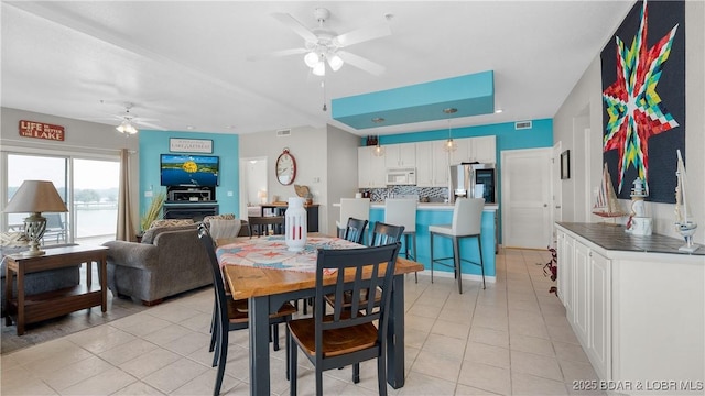 dining room with a ceiling fan, light tile patterned flooring, and a raised ceiling