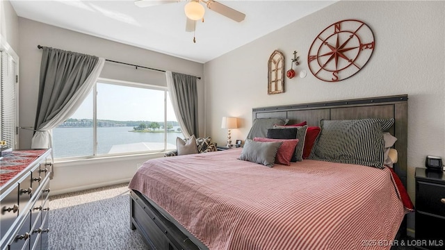 carpeted bedroom featuring a water view, a ceiling fan, and baseboards