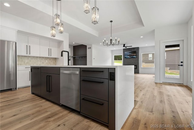 kitchen with appliances with stainless steel finishes, a chandelier, white cabinets, open floor plan, and light wood finished floors