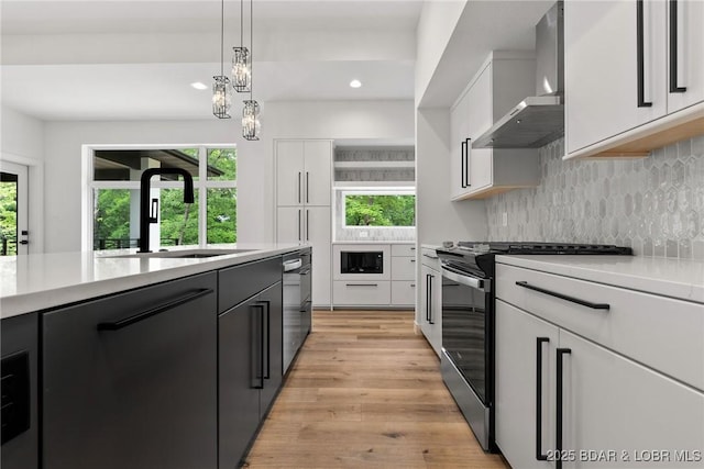 kitchen with stainless steel stove, a sink, wall chimney range hood, light countertops, and white cabinetry