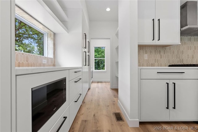 kitchen with wall chimney range hood, modern cabinets, white cabinets, decorative backsplash, and recessed lighting