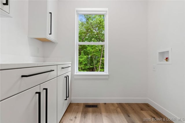 laundry area featuring cabinet space, light wood-type flooring, baseboards, and washer hookup