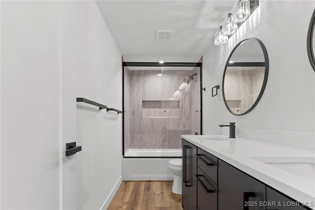 full bath with toilet, double vanity, enclosed tub / shower combo, and wood finished floors
