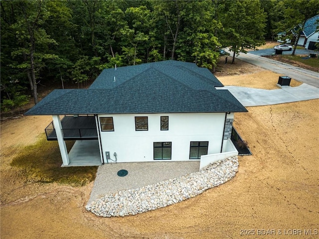 back of house featuring a shingled roof, stucco siding, and a forest view